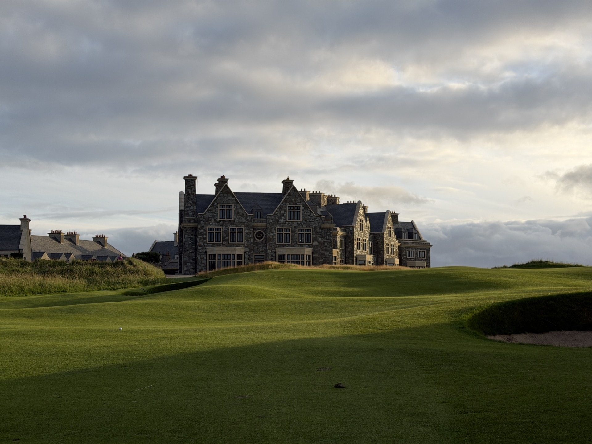 The Doonbeg clubhouse crowning the fairway — stone and slate under an Irish sky
